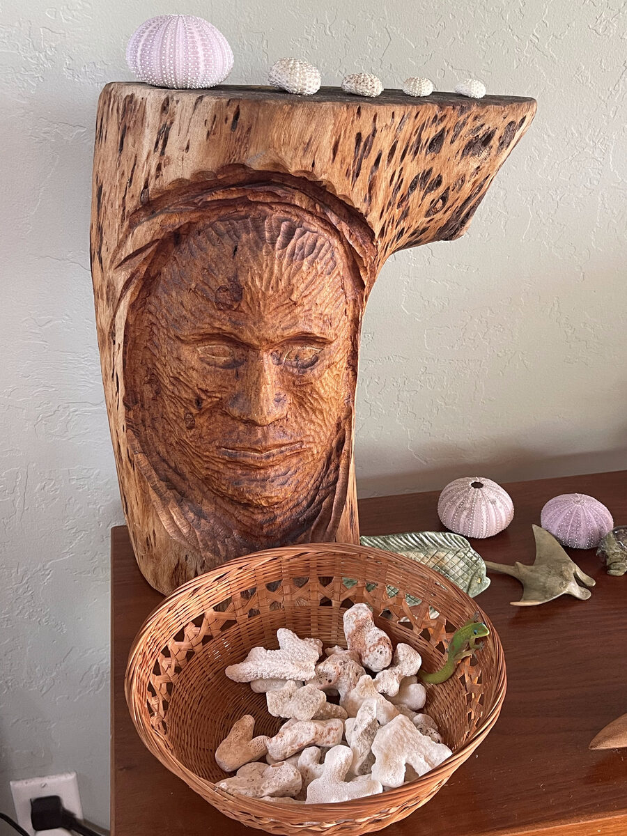 A carved Hawaiian tiki sculpture beside a woven basket of shells gathered by the founder of Holo Holo Bolo
